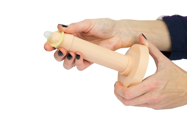 Les mains féminines déroulant préservatif sur le modèle de pénis en plastique
  - Photo, image