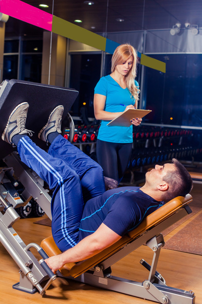 Personal trainer helping a men working out on leg press machine in gym - Foto, imagen