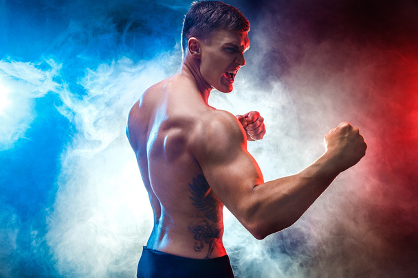 Muscular  fighter punching in smoke. Colour background. - Zdjęcie, obraz