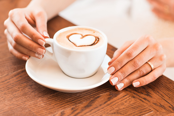 woman holding hot cup of coffee, with heart shape - Photo, Image