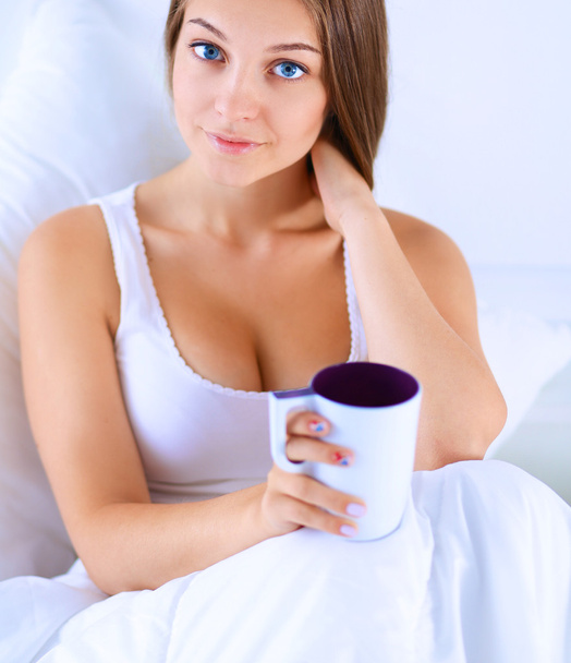 A pretty young woman in bed enjoying a cup of tea - Φωτογραφία, εικόνα