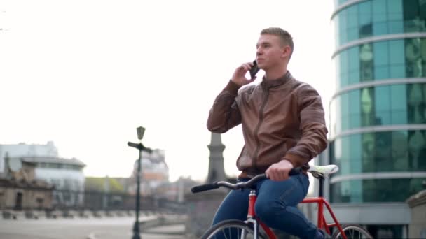 young male bicyclist talks on the phone in downtown slow motion - Materiaali, video