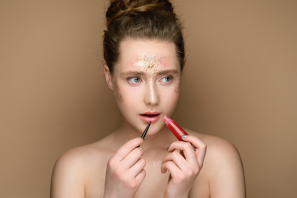 Portrait of young beautiful girl with pink lipstick in hands on the gold background. Nude makeup with tinsel and updo. Concept of the beauty. - Foto, immagini