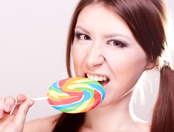 Beautiful girl with brown hair, glamorous make-up, fashion style portrait, eats candy sexy look on a gray background, smooth skin, - Φωτογραφία, εικόνα