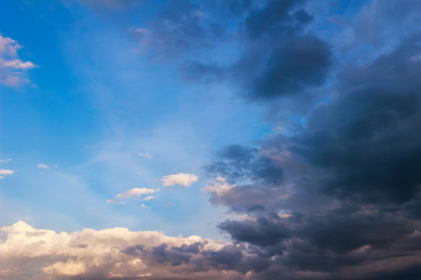 Blauwe hemelachtergrond met kleine witte, enorme donkere regenwolken. - Foto, afbeelding