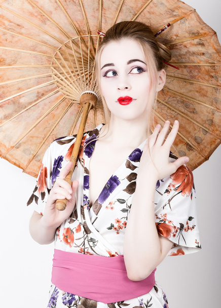 beautiful girl dressed as a geisha girl holding a Chinese umbrella. Geisha makeup and hair dressed in a kimono. The concept of traditional Japanese values - Foto, Bild