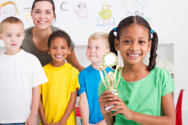 Preschool girl holding a trophy in front of classmates - Фото, зображення