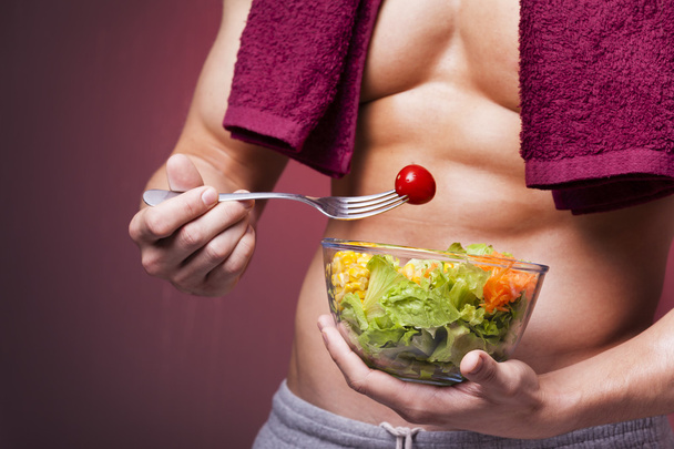 Muscular man holding a bowl of salad  - Photo, image