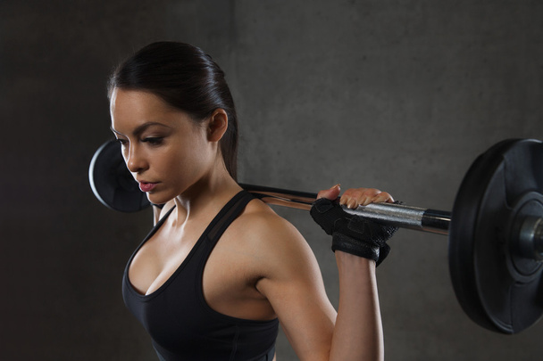 young woman flexing muscles with barbell in gym - Foto, afbeelding