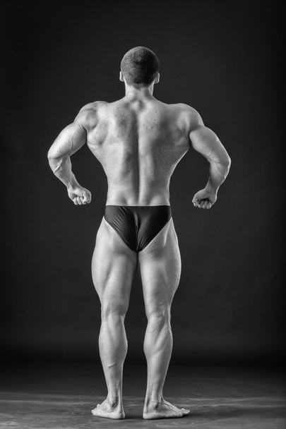 Kehonrakentaja poseeraa eri asennoissa osoittaen lihaksensa. Epäonnistuminen pimeällä taustalla. Miehen lihakset jännittyvät. Kaunis lihaksikas urheilija
. - Valokuva, kuva