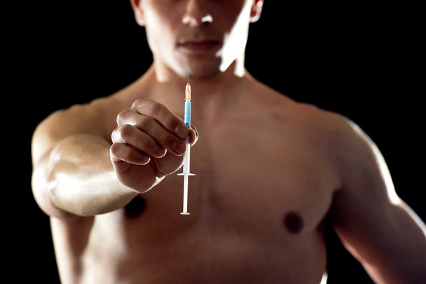 young athletic sportsman holding syringe in sport doping and cheat concept - Fotó, kép