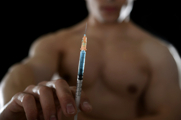 young athletic sportsman holding syringe in sport doping and cheat concept - Photo, Image