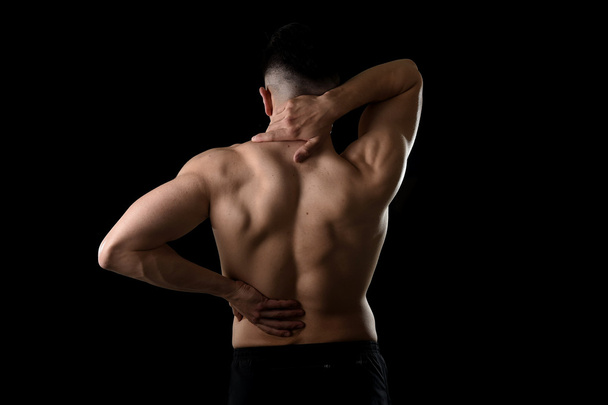 back view of young man with muscular body holding his neck and low back suffering spinal pain - Foto, afbeelding