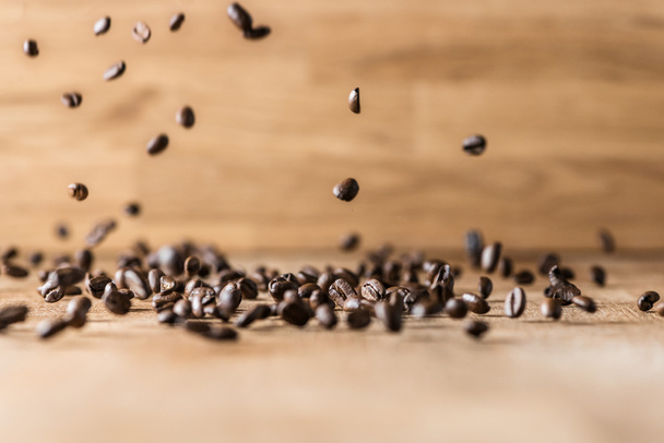 flying roasted brown coffee beans flying on wood background - Foto, afbeelding