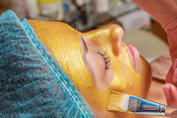 Aplicación de máscaras doradas en la cara del modelo. Procedimientos cosméticos
 - Foto, Imagen