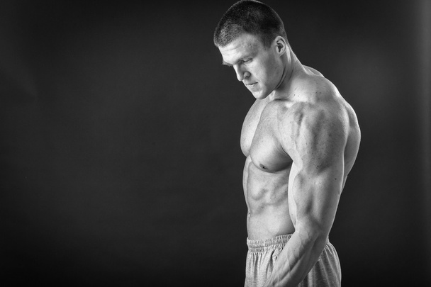 Bodybuilder poseren in verschillende poses aan te tonen hun spieren. Storing op een donkere achtergrond. Mannelijke weergegeven: spieren spannen. Mooi gespierd lichaam atleet. - Foto, afbeelding