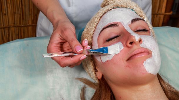 Girl with a beautician at spa salon. Beautician performs cosmetic procedures.applying cosmetic cream. Cosmetology, facial, beauty - The concept of facial skin care. Article about cosmetology. - Photo, Image