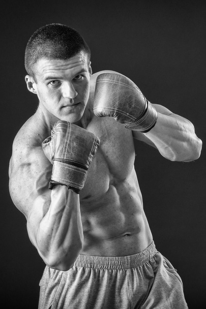 De man in bokshandschoenen. Jonge bokser vechter op zwarte achtergrond. Boksen man klaar om te vechten. Boksen, training, spiermassa, kracht, macht - het concept van krachttraining en boksen - Foto, afbeelding