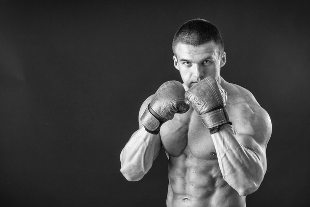 Человек в боксёрских перчатках. Молодой боксёр на чёрном фоне. Боксёр готов к бою. Бокс, тренировки, мышцы, сила, мощь - понятие силовой подготовки и бокса
 - Фото, изображение