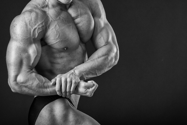 Bodybuilder posing in different poses demonstrating their muscles. Failure on a dark background. Male showing muscles straining. Beautiful muscular body athlete. - Photo, Image