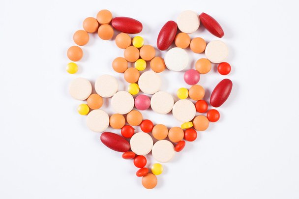 Медичні таблетки та капсули у формі серця на білому тлі, концепція охорони здоров'я
 - Фото, зображення