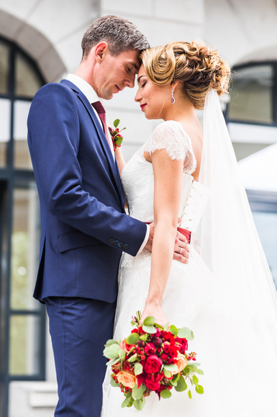 γαμήλιο ζεύγος αγκάλιασμα, η νύφη που κατέχουν ένα μπουκέτο λουλούδια, γαμπρός αγκαλιάζοντάς την σε εξωτερικούς χώρους - Φωτογραφία, εικόνα