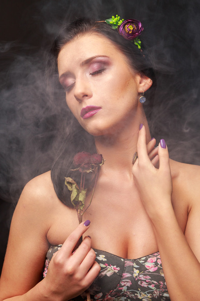 Elegante, verleidelijke brunette in een wolk van rook. Brunette in een mooie krans op een zwarte achtergrond. - Foto, afbeelding