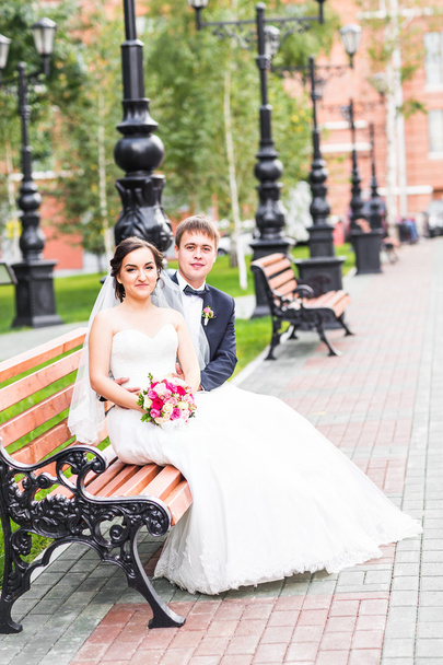 γαμήλιο ζεύγος αγκάλιασμα, η νύφη που κατέχουν ένα μπουκέτο λουλούδια, γαμπρός αγκαλιάζοντάς την σε εξωτερικούς χώρους - Φωτογραφία, εικόνα