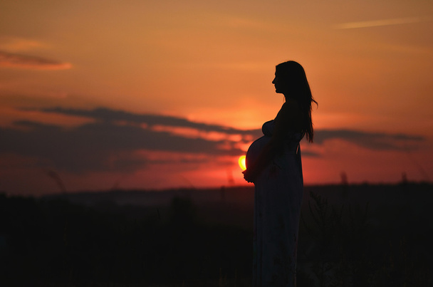 A menina grávida com um chapéu no campo de trigo em um pôr-do-sol
 - Foto, Imagem