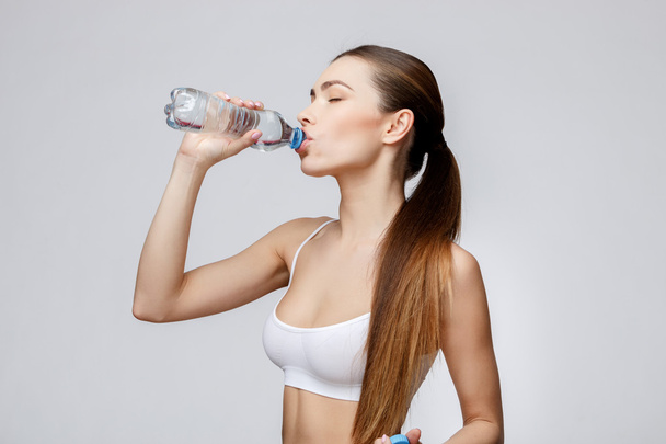 sporty woman over gray background drinking water - Valokuva, kuva