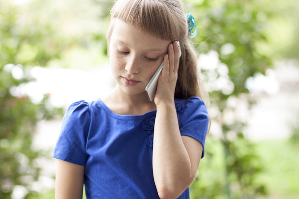 Little girl  summer park talking on the phone, in a blue dress. Blonde - Foto, afbeelding