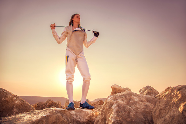 Kaya üstünde duran ve kılıcını omuzlarında tutan fencer adam - Fotoğraf, Görsel