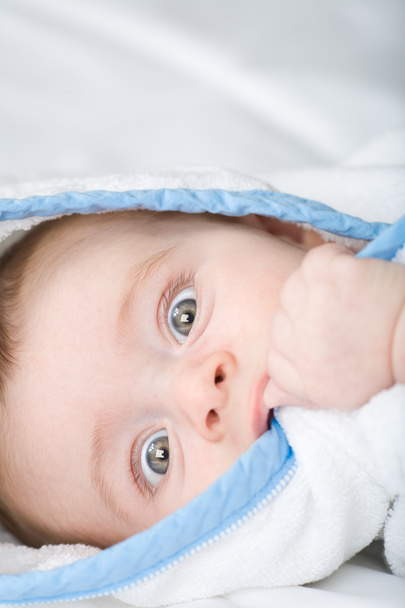 beautiful little baby with big eyes in white towel bite his hand - Foto, Imagen