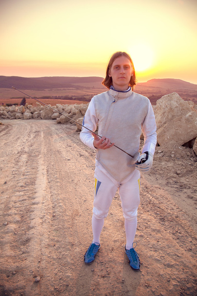 FENCER άνδρα που φοράει λευκό περίφραξη κοστούμι εκμετάλλευση σπαθί και κοιτάζοντας μπροστά - Φωτογραφία, εικόνα