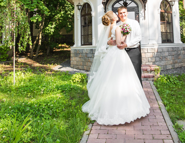 Pareja de boda abrazándose, la novia sosteniendo un ramo de flores, novio abrazándola al aire libre
 - Foto, Imagen