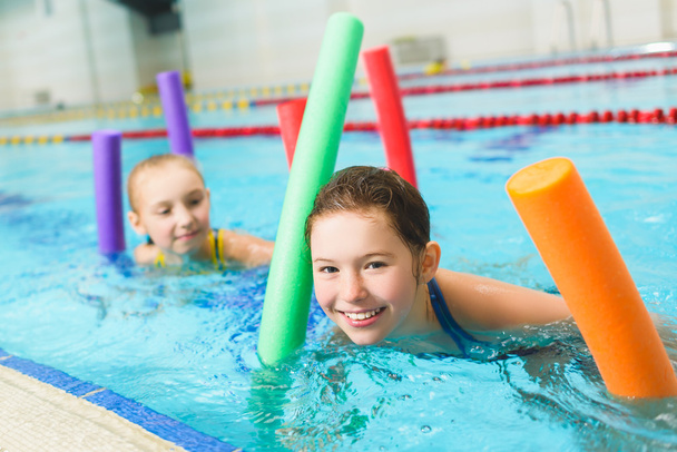 Happy and smiling group of children learning to swim with pool noodle - 写真・画像