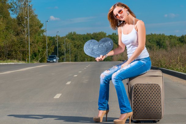 ωτοστόπ κορίτσι συνεδρίαση σε μια βαλίτσα και να περιμένει για ένα αυτοκίνητο - Φωτογραφία, εικόνα