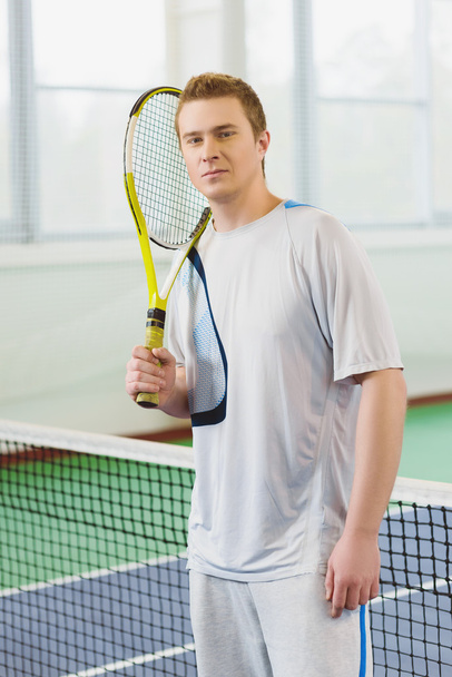 young man smiling and posing with tennis racket indoor - 写真・画像