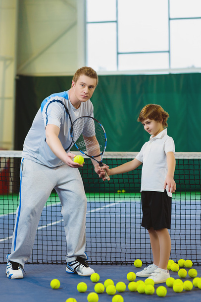 Instructor or coach teaching child how to play tennis on a court indoor - Foto, Bild