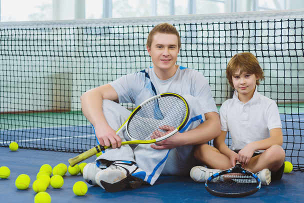 Resting young man or tennis coach with boy sitting near net - Фото, зображення