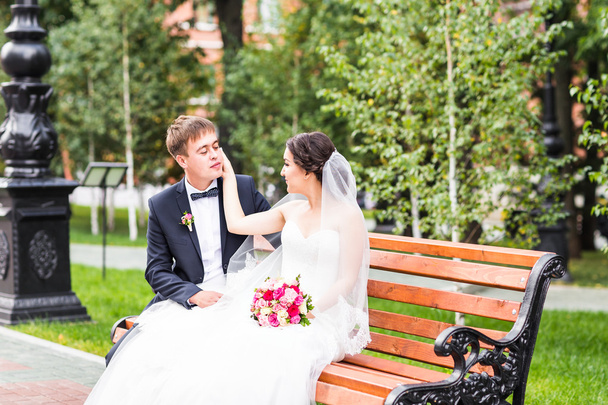 Pareja de boda abrazándose, la novia sosteniendo un ramo de flores, novio abrazándola al aire libre
 - Foto, Imagen