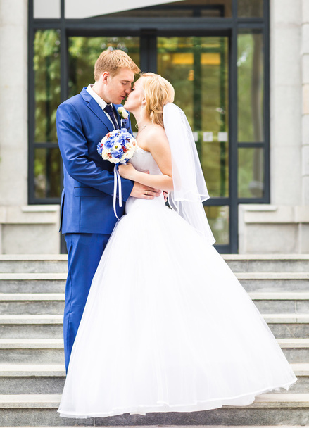 Couple de mariage câlin, la mariée tenant un bouquet de fleurs, marié embrassant son plein air
 - Photo, image