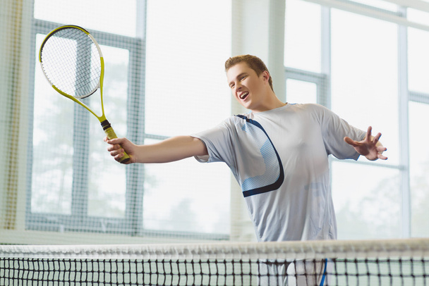 Low angle view of determined young man playing tennis indoor - Foto, Imagen