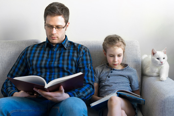 Ο πατέρας και η κόρη του διαβάζοντας βιβλία στον καναπέ. - Φωτογραφία, εικόνα