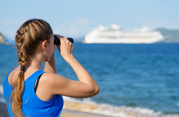 Female tourist looking through binoculars at white cruise ship - 写真・画像