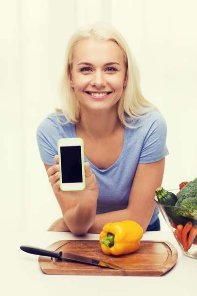 smiling woman with smartphone cooking vegetables - Valokuva, kuva
