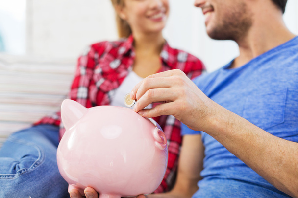 close up of happy couple putting coin to piggybank - Photo, Image