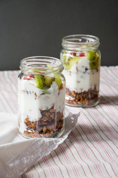 Crunchy granola in jar and yogurt parfait in glasses.  - Фото, зображення