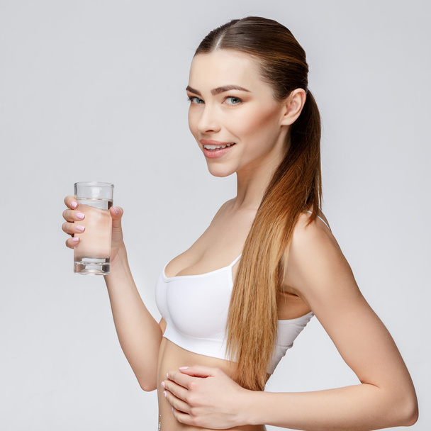sporty woman over gray background holding glass of water - Foto, Imagem