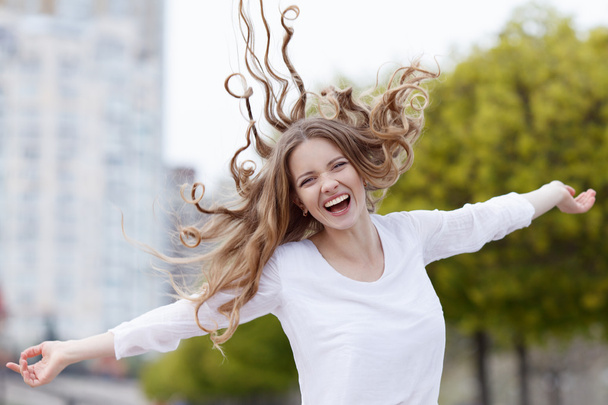 Beautiful happy smiling woman with hair flying in the sity background - Zdjęcie, obraz